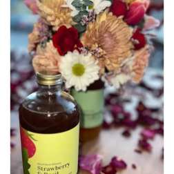Bottle of strawberry basil drink in front of a mixed flower bouquet