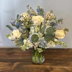 Arrangement of cream roses, blue hydrangeas, and small white flowers in a clear glass vase