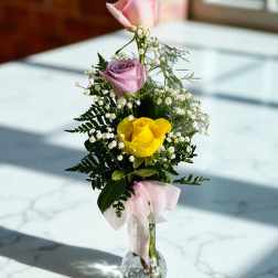 Pink, lavender, and yellow roses in a clear glass vase with a pink ribbon