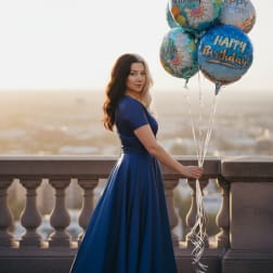 Woman in a blue dress holding a cluster of birthday balloons