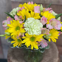 Bouquet of yellow daisies, pink alstroemeria, and white carnations in a glass vase