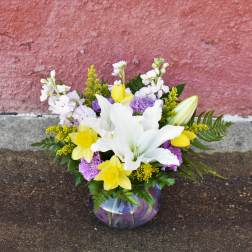 Bouquet of white lilies, yellow daffodils, and purple carnations in a glass vase