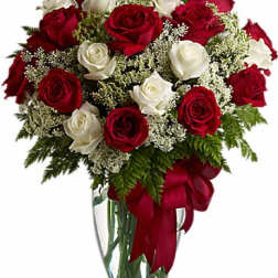 Arrangement of red and white roses with white filler flowers in a clear vase with a red ribbon bow