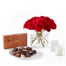 Red roses in a glass vase with chocolates and a candle