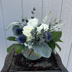 White roses in a glass vase with blue thistle and greenery