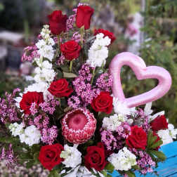 Red roses and white blooms in a vase with a pink heart pick