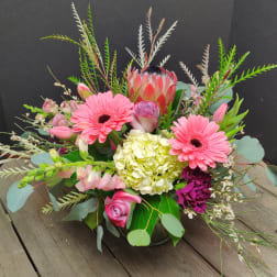 Mixed bouquet with pink gerbera daisies, roses, and a protea in a low vase