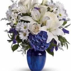 White lilies and daisies arranged in a blue vase with blue hydrangea