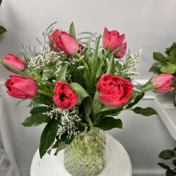 Vase of bright pink tulips with white filler flowers arranged in a textured glass vase