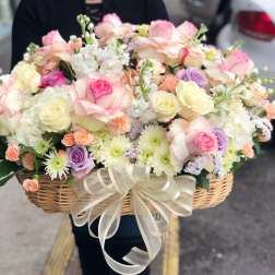 Basket of pastel roses, daisies, and small filler flowers with a ribbon bow