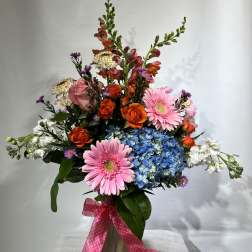 Mixed bouquet with pink gerberas, orange roses, blue hydrangea, and white blooms in a vase