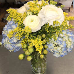 Bouquet of white ranunculus, blue hydrangea, and yellow filler in a glass vase