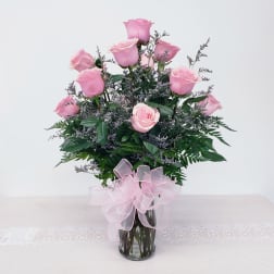 Pink roses arranged in a clear glass vase with a pink ribbon bow