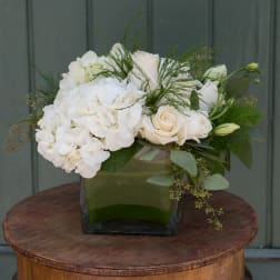 White roses and hydrangeas arranged in a square glass vase