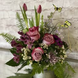 Pink roses, tulips, and mixed blooms in a silver vase with yellow butterfly picks.