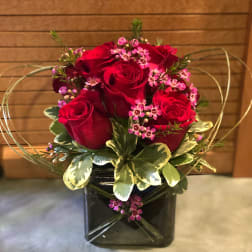 Short arrangement of red roses with small pink blooms in a black cube vase