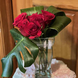 Red roses in a clear glass vase with large tropical leaves