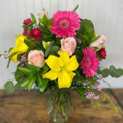 Bouquet of pink gerberas, yellow lilies, and pale roses in a glass vase