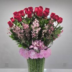 Red roses and pink flowers arranged in a clear glass vase