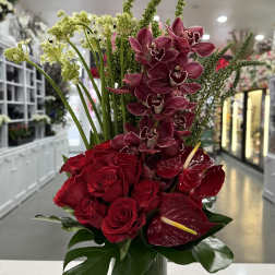 Red roses and burgundy orchids in a tall glass vase