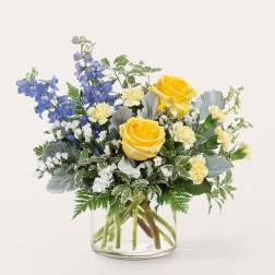 Yellow roses and blue delphinium in a clear glass vase