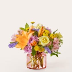 Mixed bouquet of lilies, roses, and daisies in a pink glass vase