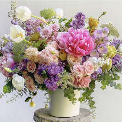 Mixed bouquet of pink, purple, and white flowers in a white vase