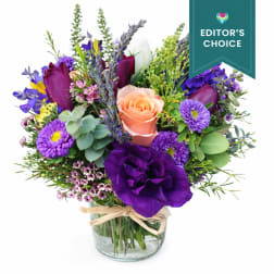 Mixed bouquet of purple and peach flowers in a clear glass vase tied with raffia