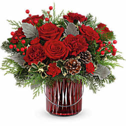 Red roses arranged in a red glass vase with pinecones and berries