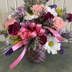 Mixed bouquet of pink, white, and purple flowers in a plaid container with a pink ribbon