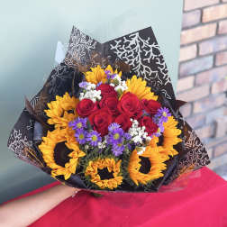 Bouquet of red roses, sunflowers, and purple daisies wrapped in black paper