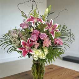 Pink lilies and roses in a glass vase with greenery