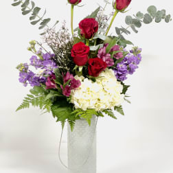 Red roses and purple flowers in a white vase
