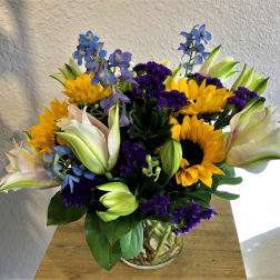 Bouquet of sunflowers, lilies, and purple flowers in a glass vase