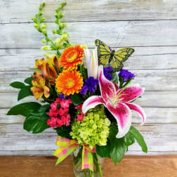 Mixed bouquet in a glass vase with orange gerberas, pink lily, and purple accents