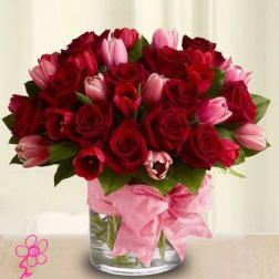 Bouquet of red roses and pink tulips in a glass vase with a pink ribbon
