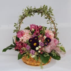 Basket arrangement of pink and purple flowers with a ribbon and arch handle