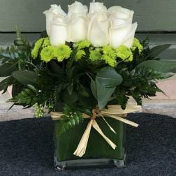 White roses and green mums in a square glass vase with a raffia bow