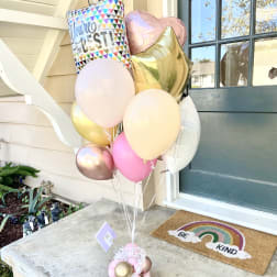 Cluster of pastel balloons with a "You're the Best" balloon and heart shapes by a front door