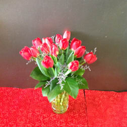 Red tulip arrangement in a yellow glass vase on a red patterned cloth