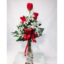 Red roses arranged with white baby's breath in a clear vase with a red ribbon