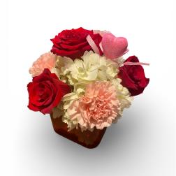 Red roses and pale carnations in a small vase with a pink heart pick