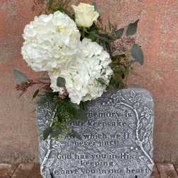White floral spray on a memorial stone with a single white rose