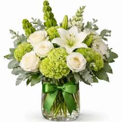 White lilies and roses with green blooms in a glass vase tied with a green ribbon
