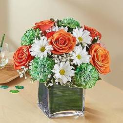 Bouquet of orange roses, white daisies, and green carnations in a square glass vase