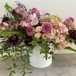 Pink and burgundy floral arrangement in a white container