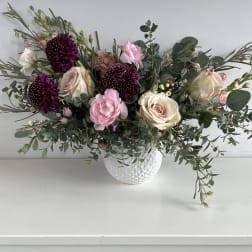Pink and cream roses with dark purple blooms in a white vase