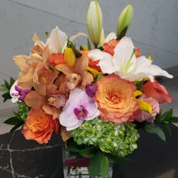 Mixed bouquet of orange roses, orchids, lilies, and hydrangea in a glass vase