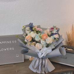 Pastel bouquet of roses, carnations, and blue flowers wrapped in gray paper