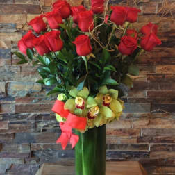 Red roses and yellow orchids in a tall glass vase with a pink ribbon
